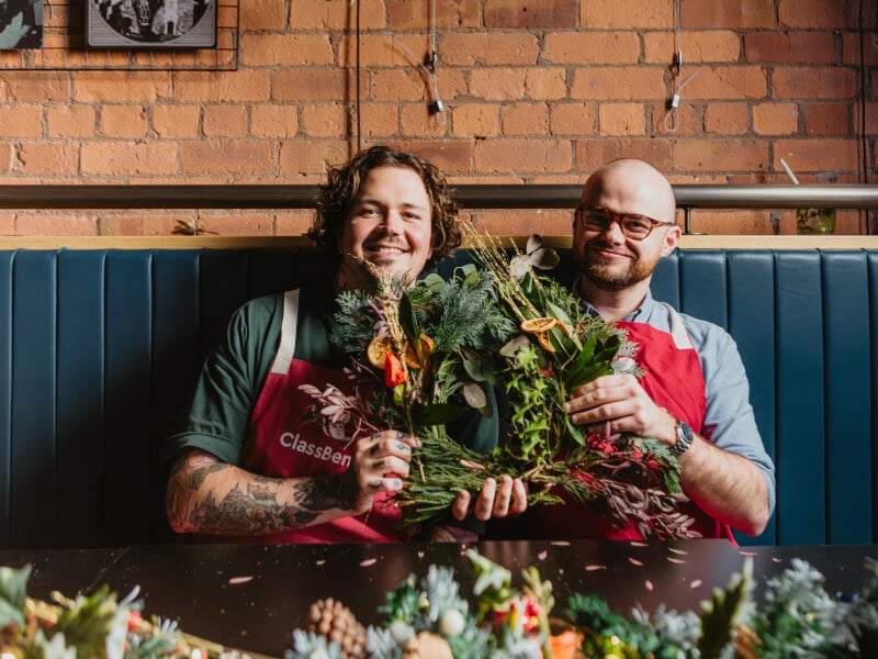 Two men holding a fresh floral Christmas wreath